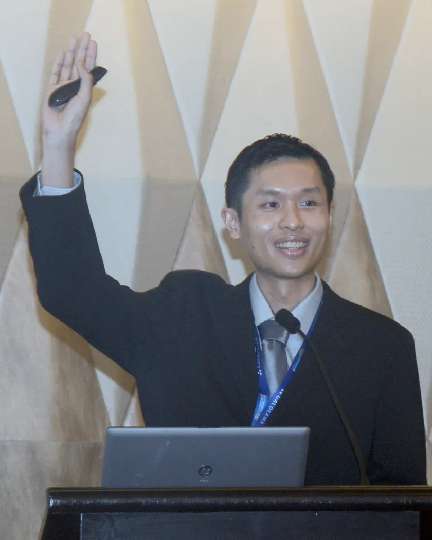Dr Eugene Tan at the lectern, smiling with his hand raised as he asks the audience a question
