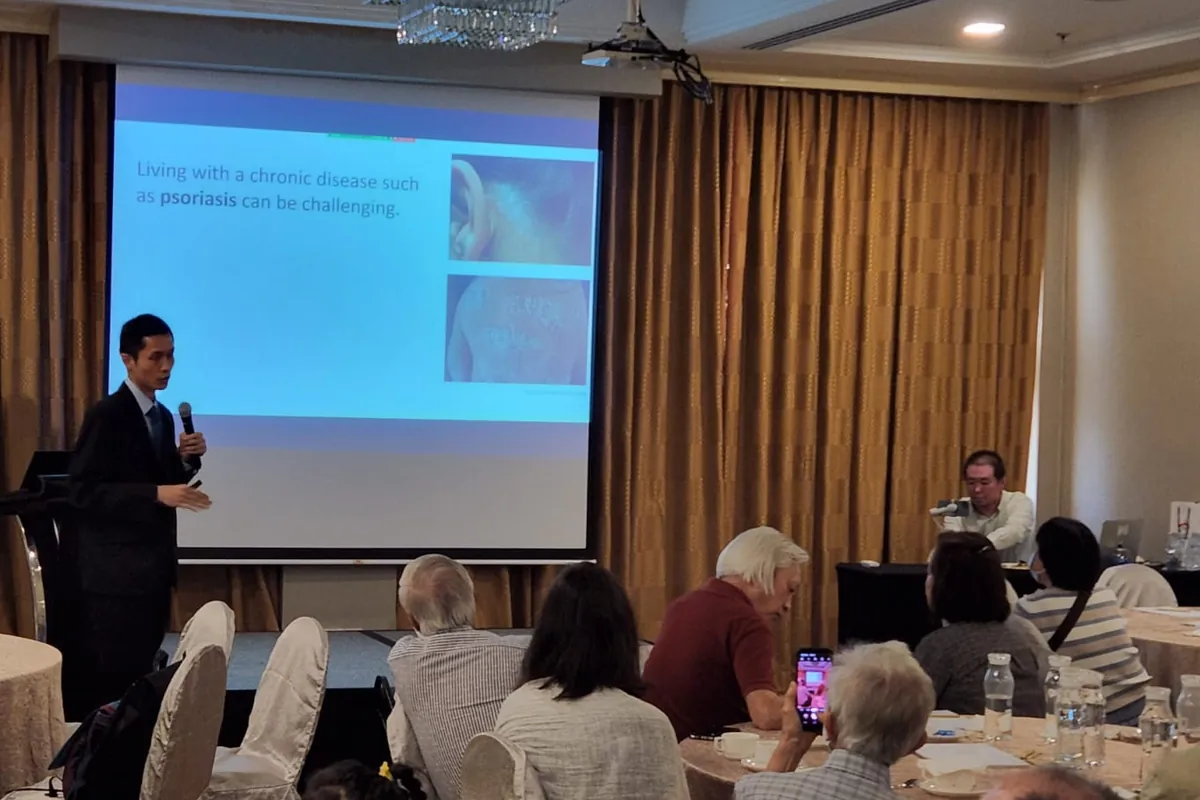 Dr Eugene Tan speaking to patients and families at a Psoriasis Association of Singapore event, beside a slide about living with psoriasis